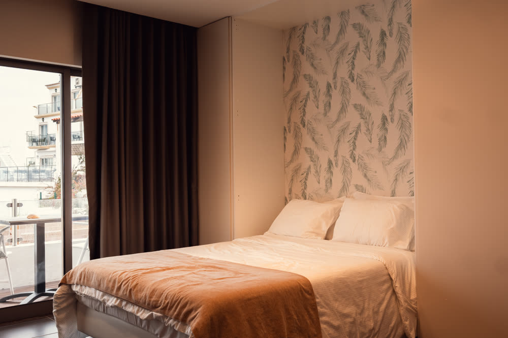 Hotel room interior in warm afternoon light, made bed and balcony doors