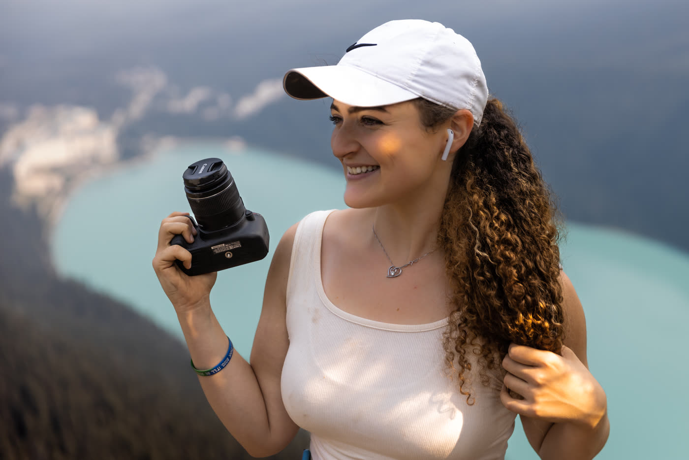 Natalie in Banff holding her camera, smiling and looking off to the side, lake below