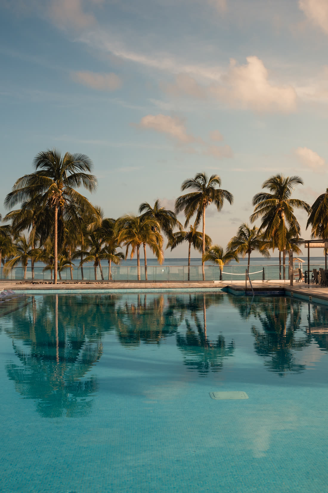 Resort pool at sunrise, palms reflected in still turquoise water