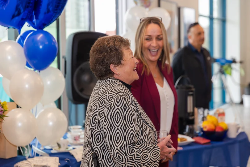 Two guests laughing during a corporate event, balloons and catering behind them