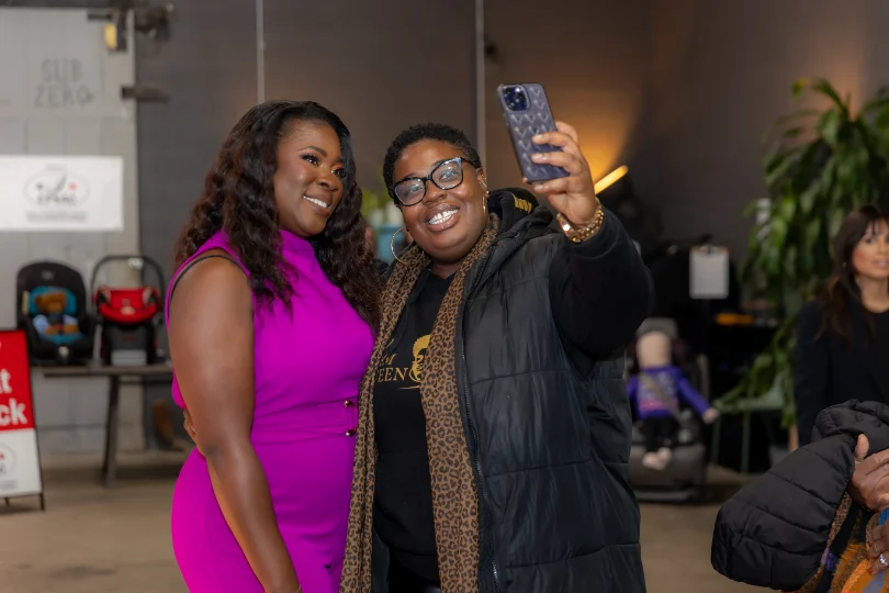 Two attendees taking a phone photo together at an indoor brand event